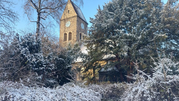 Schneebedeckte Bäume und ein Kirchturm mit Uhr im Winter
