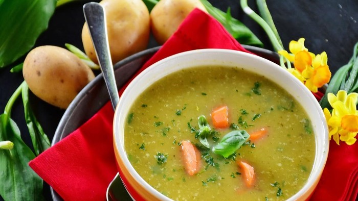 En bolle med grøn suppe med kartofler og blomster.