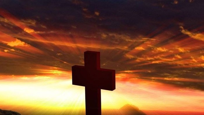 En stor rød kors på en bjergtop med solopgang i baggrunden