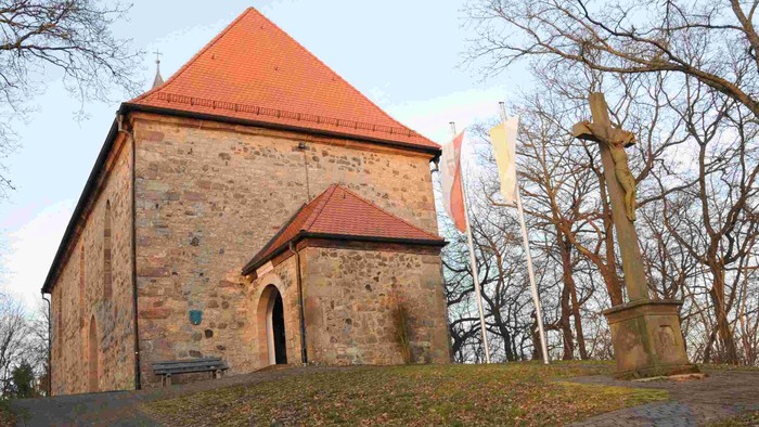 Alte Kirche mit rotem Dach und Kreuz in parkähnlicher Umgebung