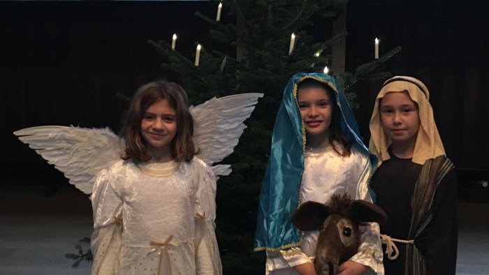 Tre piger i julekostumer foran juletree