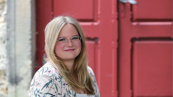 Junges Mädchen sitzt vor roter Tür und lächelt.