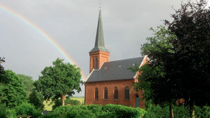Bunte Regenbogen über Kirche mit hohem Turm und grünem Dach.