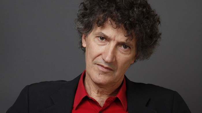 Homme aux cheveux bouclés portant une veste noire et une chemise rouge.