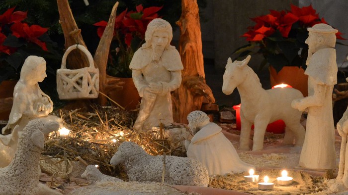 Eine Weihnachtskrippe mit Figuren, Tieren und Kerzen, vor einem geschmückten Baum