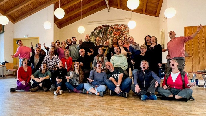 Eine große Gruppe von Menschen posiert in einem Raum mit Holzboden und Deckenlampen.