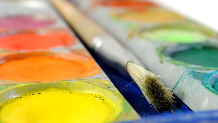 Ein Pinsel taucht in eine lebendige Aquarellpalette mit verschiedenen leuchtenden Farben ein.