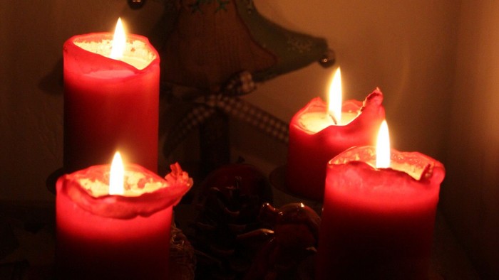 Drei brennende rote Kerzen vor einer Weihnachtskrippe