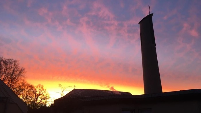 Ein hoher Schornstein vor einem Sonnenuntergang mit rosa und orangefarbenen Wolken