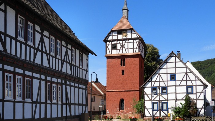 Traditionelle Fachwerkhäuser mit einem Uhrturm auf einem malerischen Dorfplatz.