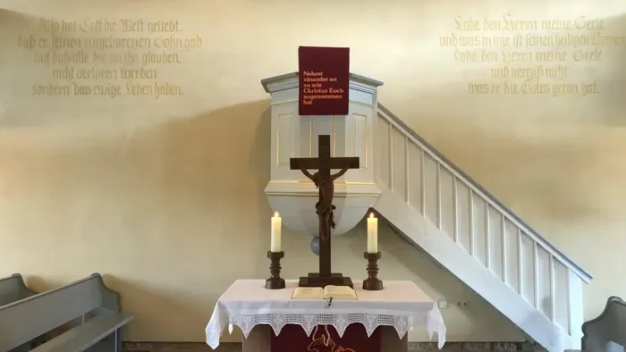 Kirchenaltar mit Kreuz, Kerzen und religiösem Text an der Wand