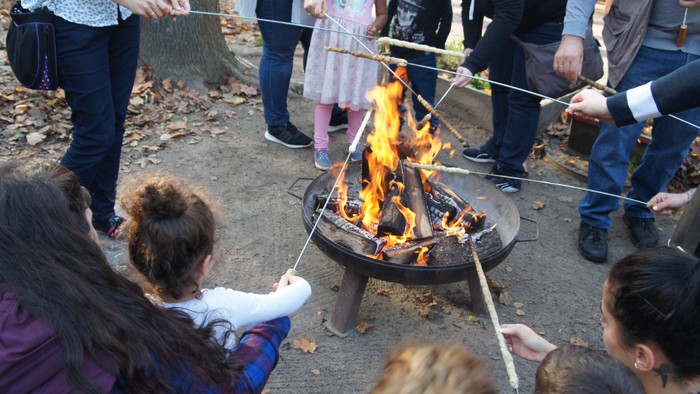 Feuerschale mit Menschen die Stockbrot ins Feuer halten.
