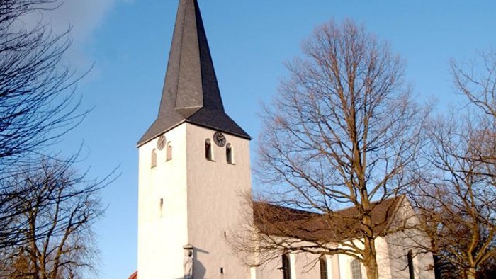 Weiße Kirche mit hohem Turm und spitzem Dach vor blauem Himmel