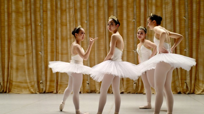 Vier Balletttänzerinnen in weißen Tutus proben auf der Bühne.