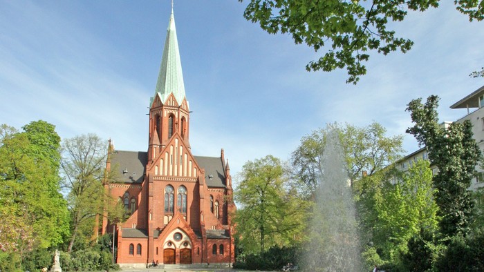 Ein rotes Kirche mit hohem Turm und ein Brunnen im Vordergrund