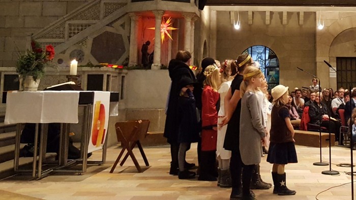 Eine Gruppe von Menschen singt in einem großen Raum, begleitet von einem Pianisten.