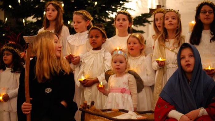 Kinderchor singt Weihnachtslieder in weißen Kleidern und mit Kränzen