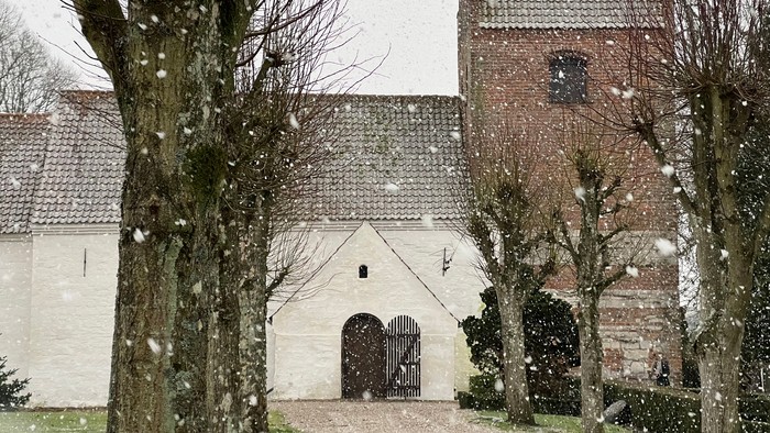 En snødekkede kirke med tårn og træer.