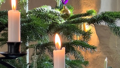 En lille julestænde med tre lysende lysekønge og lilla pynt.