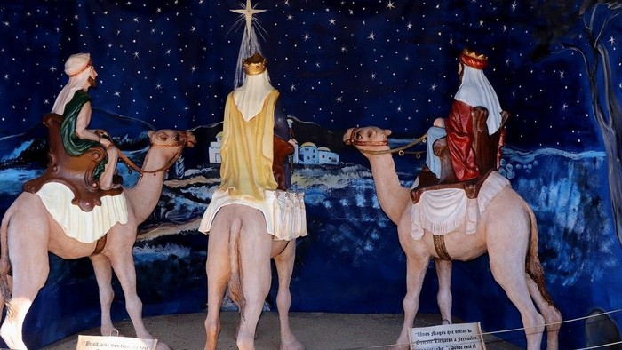 Three wise men on camels, each holding gifts, against a starry night backdrop.