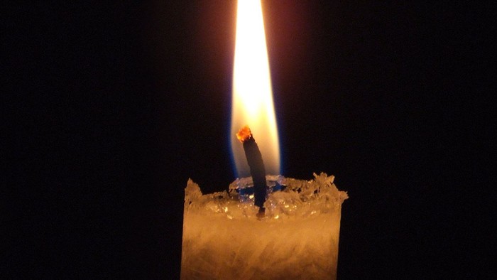 Single lit candle in darkness.