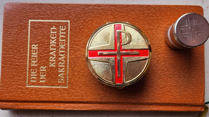 Das Bild zeigt ein hölzernes Reliquiar mit einem roten Kreuz und einem Zylinder.