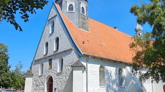 Kleine weiße Kirche mit rotem Dach und Turm auf grünem Rasen