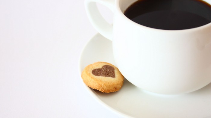 Eine Tasse Kaffee und ein Herzkeks auf einem Teller