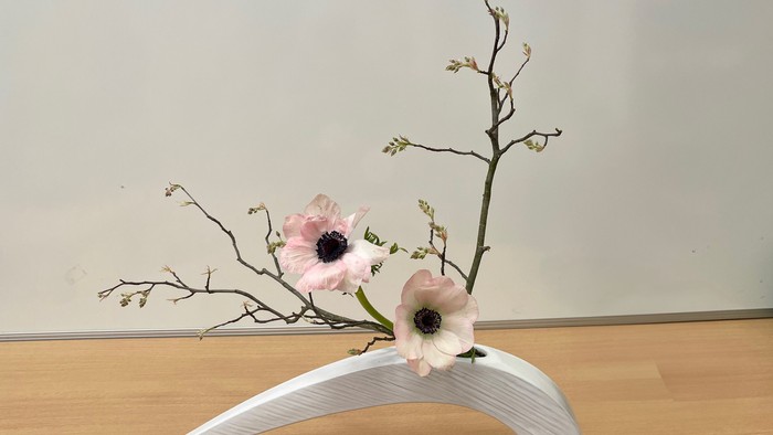 Ein weißer Blumenhalter mit zwei rosa Blumen auf einem Holzboden