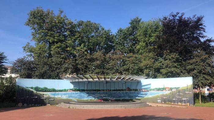 Modernes Gebäude mit Glasfassade und überdachter Terrasse, umgeben von Bäumen und Grünflächen