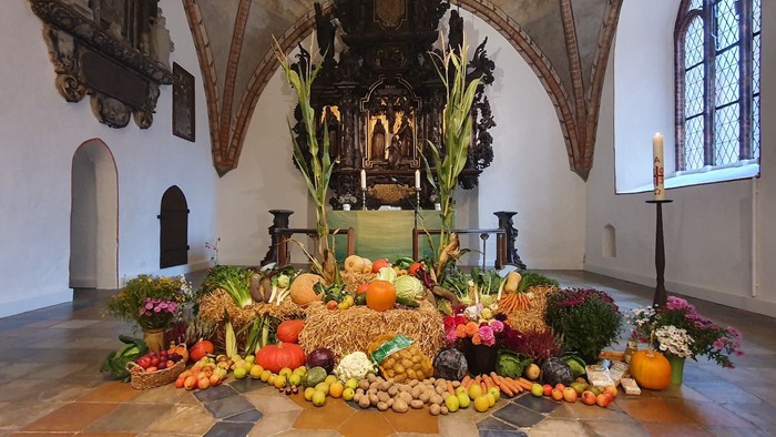 Bunte Obst- und Gemüsesammlung in Kirchenraum mit Altar und Kerzenleuchter