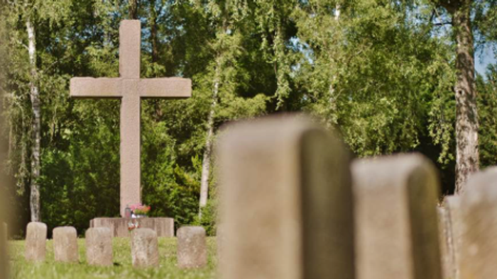 Ein großes Kreuz mit einem Blumenstrauß davor, dazu etliche andere Grabsteinen auf dem Friedhof Schleswiger Straße