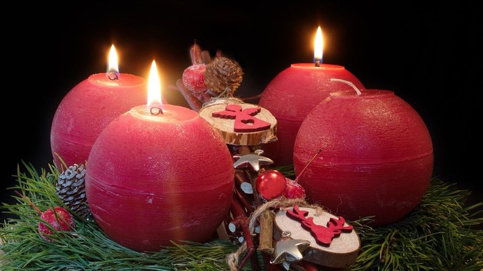 Drei rote Kerzen in Adventskranz mit Tannenzweigen und Weihnachtsdekoration