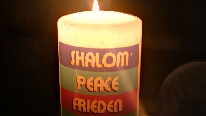 Das Bild zeigt eine Kerze mit der Aufschrift Schalom, Peace und Frieden. 