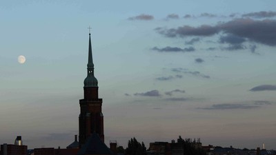 Ein hoher Kirchturm vor einem bewölkten Himmel bei Dämmerung