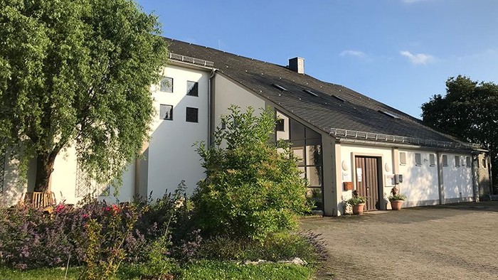Das Bild zeigt ein weißes Haus mit Garten und Bäumen unter blauem Himmel.