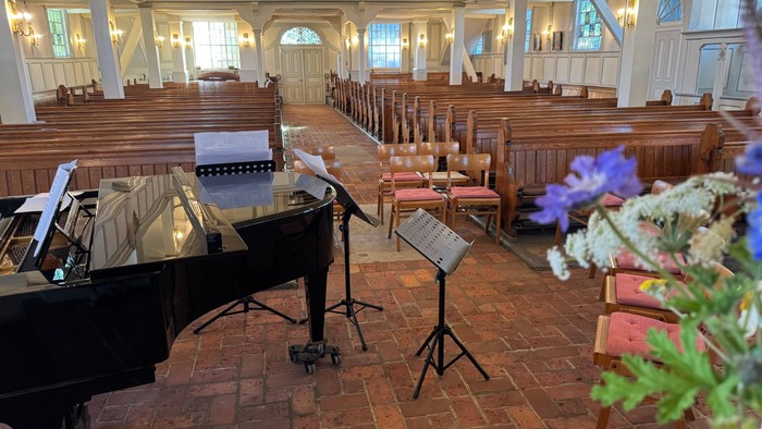 Elegante Kircheninnenausstattung mit einem Flügel, Kirchenbänken und Blumendekorationen auf einem Ziegelboden.