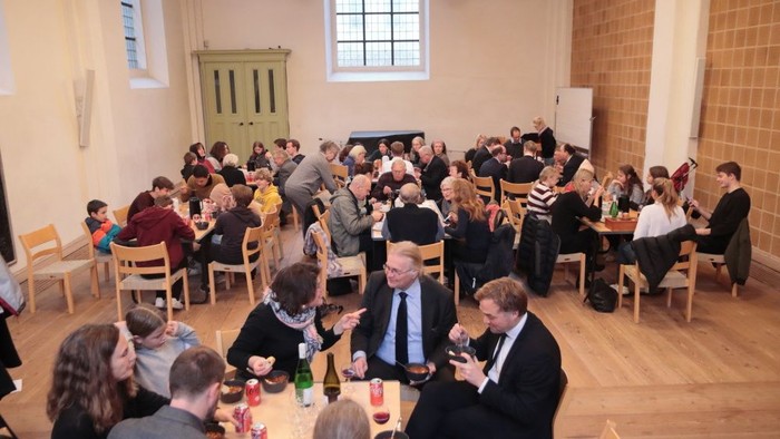 Eine Gruppe von Menschen sitzt an Tischen in einem Raum und isst.