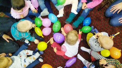 Eine Gruppe Kinder sitzt auf dem Boden und spielt mit bunten Luftballons.