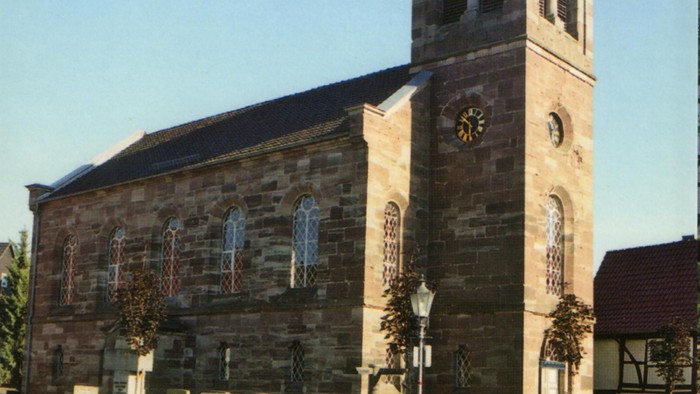 Kirche mit hohem Kirchturm und Kreuz an der Spitze vor klarem blauen Himmel.