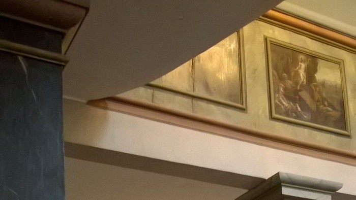 Ein Metallhahn steht in einem Raum mit Marmorsäulen und einem Gemälde an der Wand