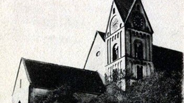 Alte Kirche mit hohem Turm und Uhr, umgeben von Bäumen