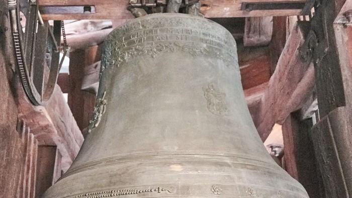 Ein großer, alter Glocke hängt in einem hölzernen Turm.