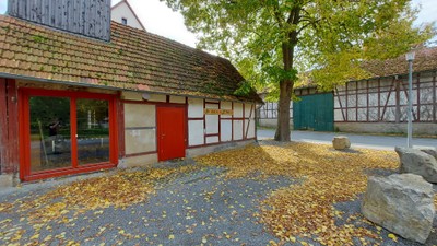 Herbstblätter bedecken den Boden vor einem traditionellen Haus mit roten Türen und einem strohgedeckten Dach.