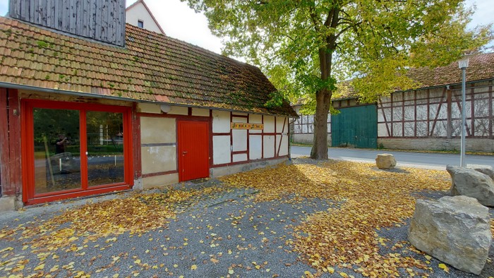 Herbstblätter bedecken den Boden vor einem traditionellen Haus mit roten Türen und einem strohgedeckten Dach.