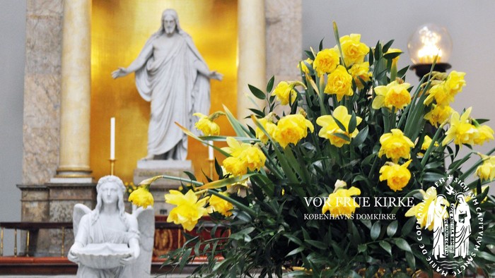 En kirkeinterior med statue af Jesus og gule blomster.