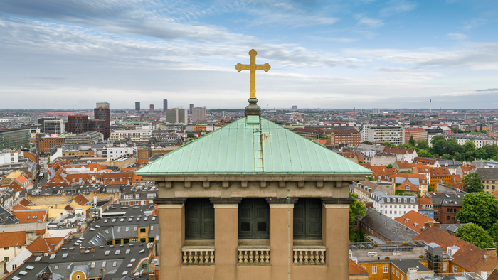Bygning med tårn og guld cruz på toppen, ud over en stor by med mange røde tag.