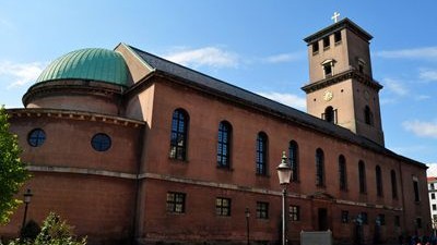 En rød murstenskirke med grøn kuppel og tårn.