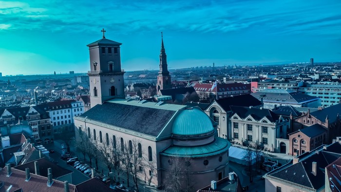 Bybillede med fremtrædende kirkebygninger under blå himmel.