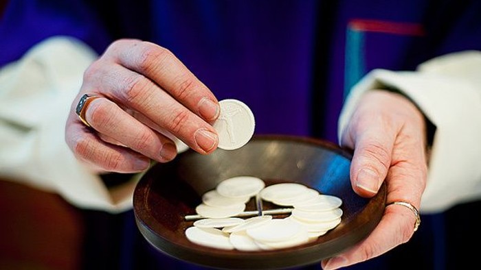 Hænder holder en skål med hostier og en mynt.